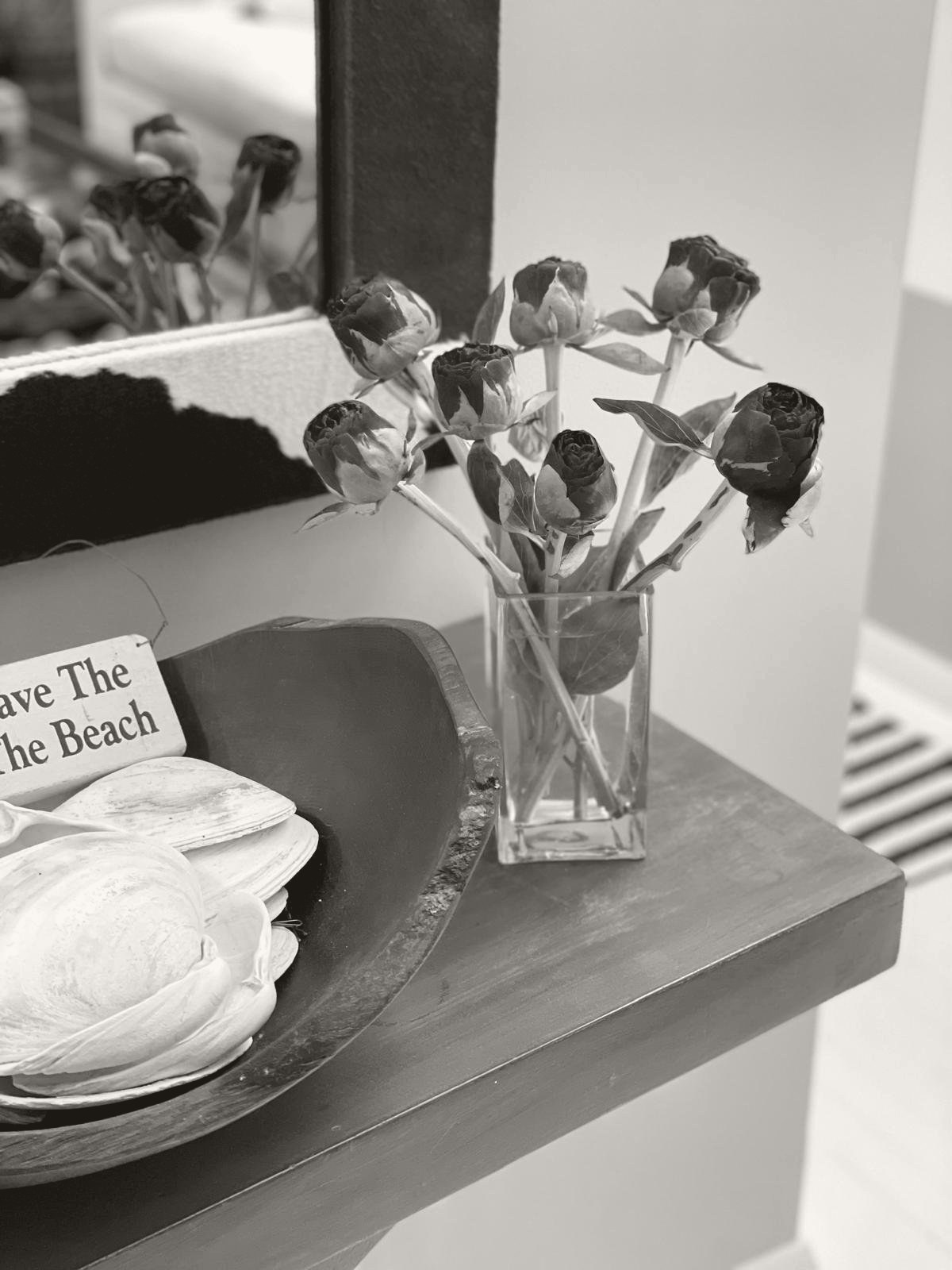 A still life in a private home, peony buds in a glass vase beside a bowl of shells
